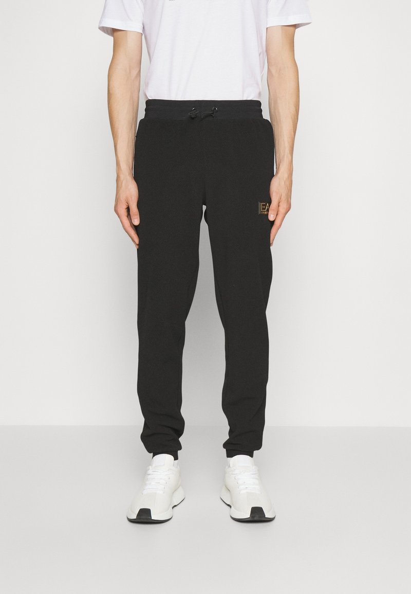 Svarta joggingsbyxor i ett strukturerat tyg, med elastisk midja och dragsko. Liten detalj med guldlogotyp på framsidan.