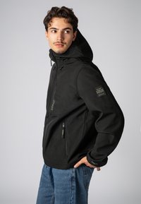 Zwarte hoodie met een matte afwerking, ritszakken en een patch op de mouw. Draag het over blauwe denim broek met een casual snit.