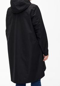 Person wearing a long black hooded raincoat from the back, standing against a plain white background.