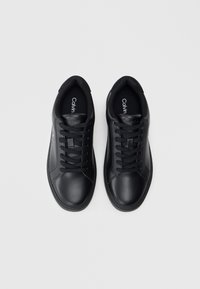 Μαύρα συνθετικά σνίκερς με λεία υφή, στρογγυλή μύτη και μαύρες κορδόνες. Ο λογότυπος "Calvin" ορατός στο εσωτερικό. Κλασικός αθλητικός σχεδιασμός.