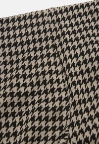 Beige stof met een zwart houthakkermotief, met een diagonale vouw en een textuurgebreide detail.