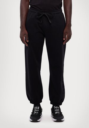 Black sweatpants made of soft fabric with an elastic waistband, drawstring, and cuffed hems, featuring side lettering accents.