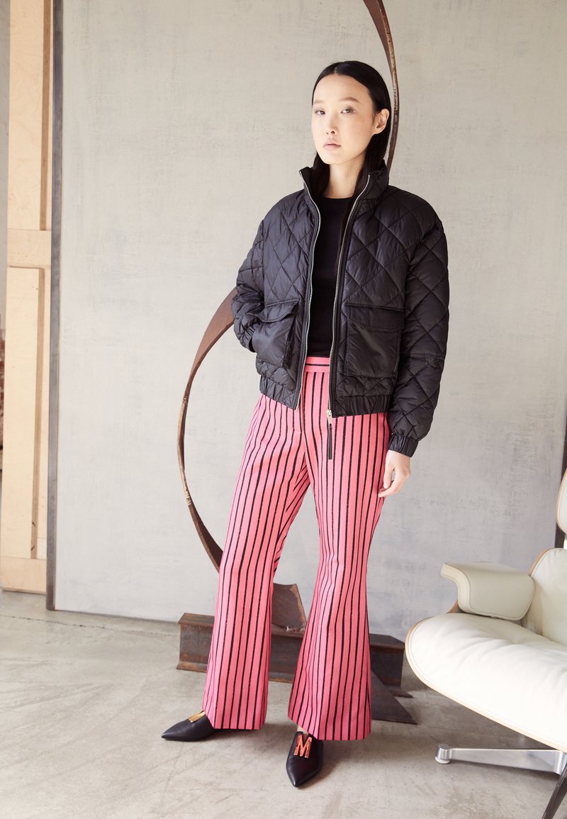 Jaqueta bomber preta com acolchoado e fecho zipp, combinada com calças flare listas em rosa. Tecido elegante, sapatos de cor sólida com um detalhe em forma de 'M'.
