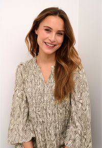 Light brown marble-patterned dress with a V-neck, gathered waist, and flared sleeves. Smooth texture against a neutral background.
