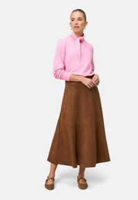 Pink knitted sweater with a tied neckline, paired with a brown suede midi skirt. The outfit features long sleeves and a flared design.