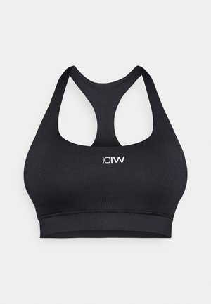 Schwarzer Sport-BH mit Racerback-Design, hergestellt aus dehnbarem Stoff. Verfügt über dekorative Nähte und ein vorne aufgedrucktes Logo.