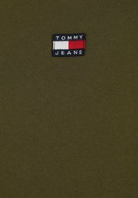Camiseta verde oliva hecha de tela acanalada que presenta un parche con el logo "TOMMY JEANS" y acentos en bloques de color rojo y blanco.