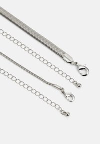 Zilveren kettingaccessoire met een golfstructuur, bestaande uit twee kettingsegmenten en kreeftsluitingen. Kenmerkt zich door ronde schakels en een gladde metaafwerking.