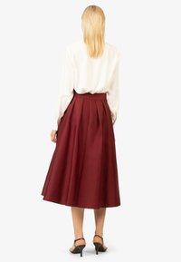 Gonna midi plissettata bordeaux realizzata in un tessuto morbido, abbinata a una blusa bianca. Presenta una vita sagomata e tacchi con cinturino alla caviglia.