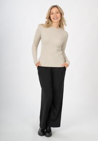 Beige geripptes Langarmoberteil kombiniert mit locker sitzenden schwarzen Hosen und schwarzen Ankle Boots, mit einem schlichten runden Halsausschnitt.