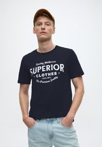 Navy blue cotton t-shirt with short sleeves, featuring white graphic text reading "SUPERIOR CLOTHES" and vintage-style accents.