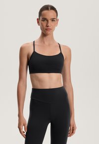 Musta urheiluliivit, joissa on ohuet säädettävät hihnat, saumaton muotoilu, pehmeä pinta ja leveä tukivyö. Yhdistetty korkeavyötäröisiin leggingseihin.