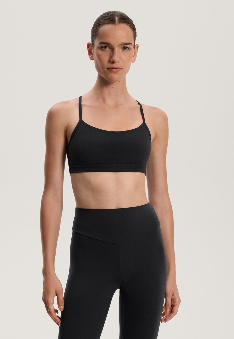 Černá sportovní podprsenka s tenkými nastavitelnými ramínky, bezešvým designem, měkkou texturou a širokým lemem pro podporu. Kombinována s legínami s vysokým pasem.