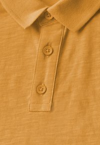 Polo jaune en tissu texturé, avec un col structuré et trois boutons de fermeture. Les boutons sont ronds et légèrement surélevés.