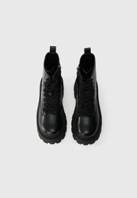 Czarne skórzane botki za kostkę z teksturowanym wykończeniem, okrągłym czubkiem i grubą, trwałą podeszwą. Posiadają sznurowadła oraz zamek błyskawiczny z boku dla łatwego zakładania.