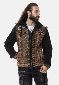 Schwarze Kapuzenjacke kombiniert mit einer abgenutzten braunen Jeansjacke. Verfügt über Fronttaschen, einen Reißverschluss und dekorative Patches auf den Schultern.