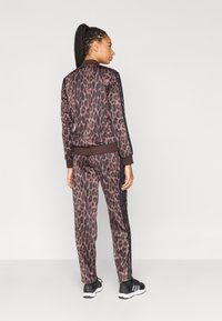 Dres w panterkę w ciemnym brązie i czerni, składający się z kurtki na suwak oraz dopasowanych spodni, oba z ściągaczami na rękawach i nogawkach oraz paskami po bokach.