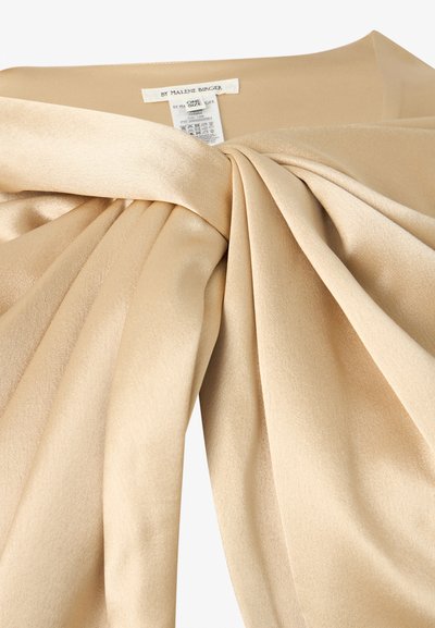 Μπεζ σατέν μπλούζα με λεπτομέρεια κόμπου στο μπροστινό μέρος και ορατή ετικέτα της μάρκας "By Malene Birger" στο λαιμόκοψη.