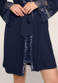 Granatowy szlafrok z koronkowym wykończeniem rękawów i brzegów. Wykonany z lekkiego materiału, z paskiem w talii, ozdobiony delikatnym kwiatowym wzorem.
