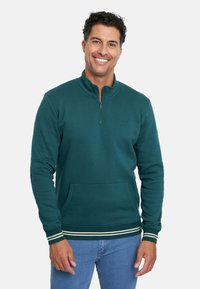 Sudadera de color verde azulado oscuro con cuello de media cremallera, bolsillo frontal y puños de canalé a rayas blancas. Tejido suave con un branding mínimo.