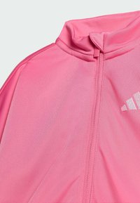 Różowa kurtka sportowa z wysokim kołnierzem, zapięciem na zamek i teksturowanym materiałem. Posiada subtelne logo w białym kolorze po lewej stronie.