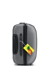 Grijze harde koffer met een gestructureerd oppervlak, zwarte rits, zijhandvat en een kleurrijke ananas-vormige bagagelabel eraan bevestigd.