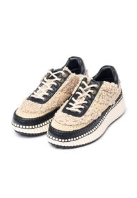 Beige und schwarze Sneakers mit einem strukturierten, flauschigen Obermaterial, glatten Lederdetails, dicker Sohle mit geriffeltem Muster und kontrastierenden Nähten.