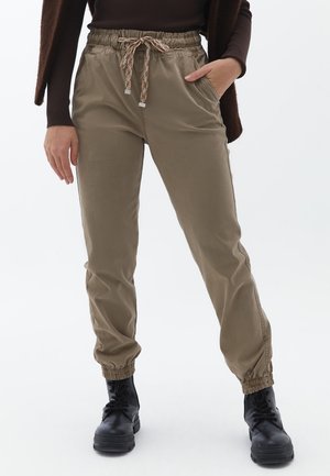 Pantaloni jogger color khaki con vita elastica e cordino, dotati di tasche laterali e polsini arricciati. Il materiale ha una consistenza liscia.