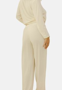 Ensemble de loungewear côtelé crème comprenant un haut à manches longues et un bas à jambes larges. Texture douce avec une coupe décontractée ; détails de design minimalistes.