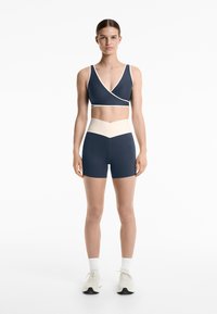 Navy och krämfärgad träningsklädesset som innehåller en sport-bh med omslagsstil och högmidjade shorts med en färgblockssdesign och slät textur.
