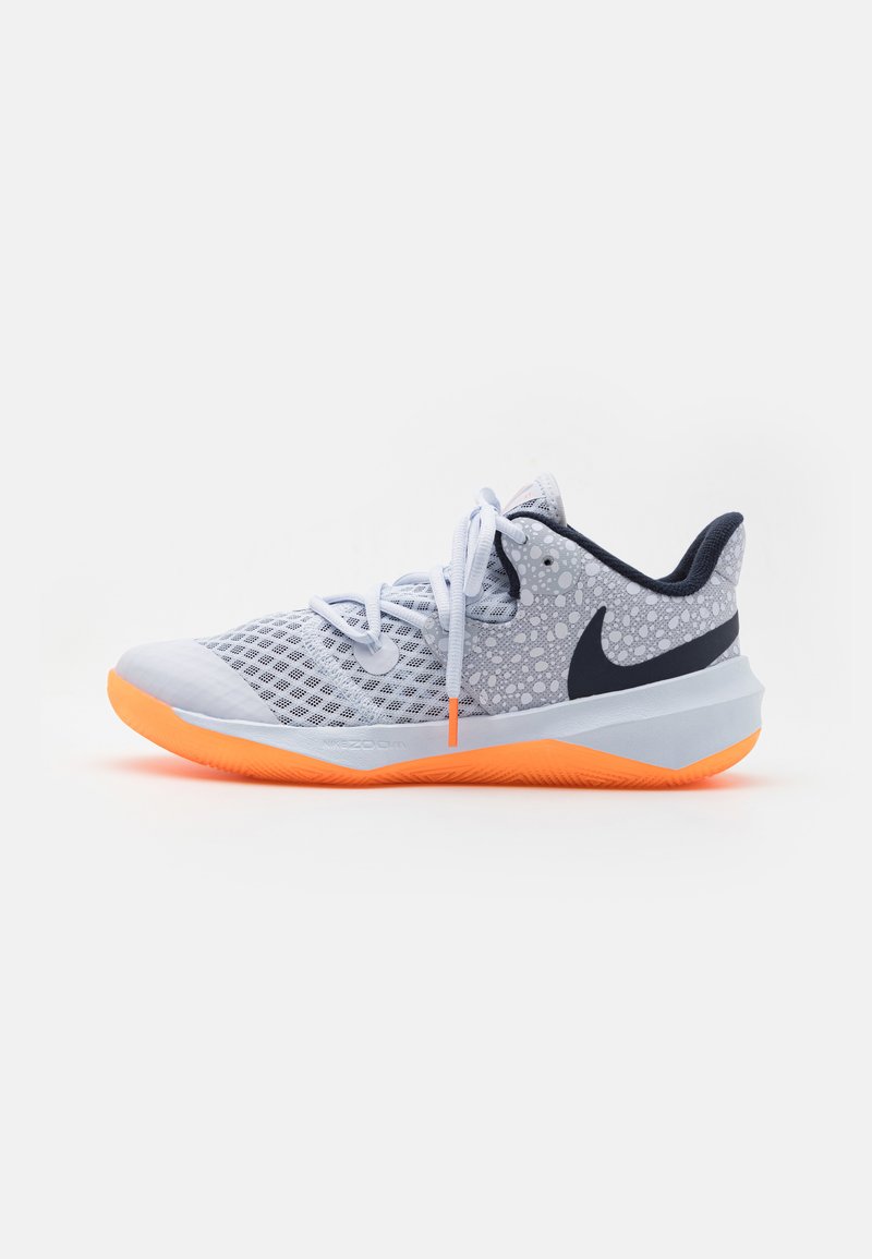 Chaussure de sport bleu clair avec une tige en maille, détails mouchetés blancs et gris, accents bleu marine et semelle en caoutchouc orange vif. Lacets inclus.