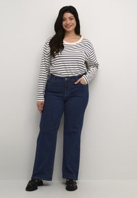 Top de rayas de manga larga en crema y azul marino, combinado con unos pantalones vaqueros de pierna ancha y cintura alta en azul oscuro. Modelo lleva unos zapatos de plataforma negros.