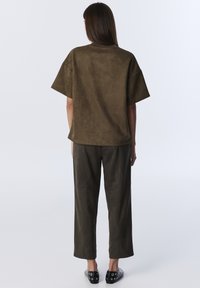 Olijfgroene suede top met korte mouwen, gecombineerd met bijpassende wijde broek. Heeft een gladde textuur en een simpel ontwerp.