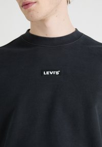 Svart sweatshirt gjord av bomull. Har rund hals och en lapplabel med texten "LEVI'S" i vitt på bröstet. Slät textur.