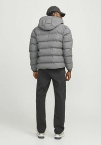 Grå pufferjakke med hætte, quiltet design og ribbede manchetter, parret med sorte cargo-bukser og hvide sneakers.