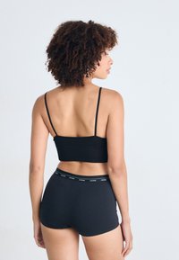 Camisole noire à côtes avec des bretelles fines, assortie à un short noir avec un bandeau logo à la taille, vue de dos.