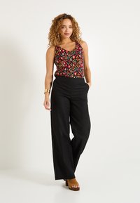 Top sin mangas con estampado floral en colores vibrantes, combinado con pantalones negros de tiro alto y perneras anchas, y tacones de plataforma marrones.