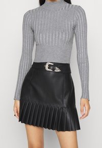 Pull à col roulé gris côtelé associé à une jupe plissée en similicuir noir avec une boucle argentée décorative sur la ceinture.