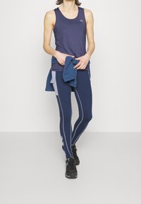 Tummansininen toppi, jossa on pyöreä kaula-aukko ja logo, yhdistettynä yhteensopiviin tiukkoihin legginsseihin, joissa on vaaleanharmaat pystysuorat raidat ja yksityiskohtia.