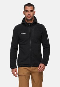 Black fleece jacket with a hood, full zip front, textured surface, and logo on the chest. Features a zippered chest pocket and elastic cuffs.