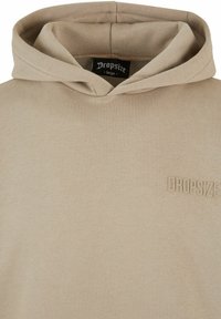 Beige hættetrøje lavet af blødt stof, med et tekstureret "DROPSIZE" logo på venstre bryst. Omfatter en klassisk, afslappet pasform.