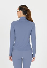 Langarm-Sportoberteil in Hellblau, aus glattem, dehnbarem Material. Mit hohem Kragen und figurbetontem Design mit Raglanärmeln.