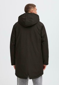 Mørk, hetteparkas med en strømlinjeformet design, som har en matt overflate og en lett forlengt snitt, passende for kaldt vær.