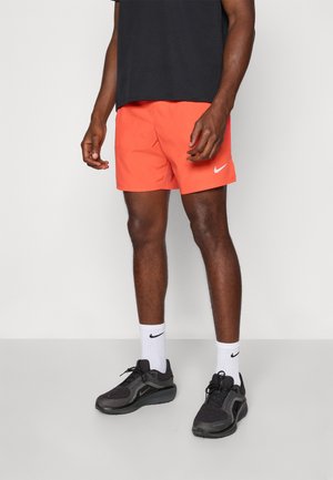 Herren-Shorts von Nike in Orange mit einem weißen Logo, kombiniert mit schwarzen Schuhen und weißen Socken. Schlichtes Design und leichtes Material.