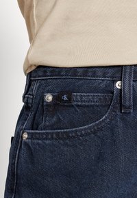 Mörkblå denimjeans med en slät yta och en subtil tvätteffekt, med silverfärgade detaljer och en svart cK-logotagg på fickan.