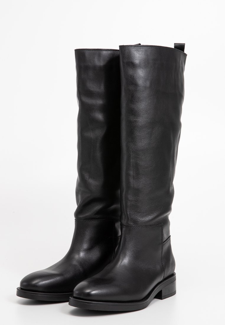 Ein Paar hohe schwarze Lederstiefel mit niedrigen Blockabsätzen und runden Zehen, die auf einem weißen Hintergrund aufrecht stehen.