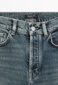 Jeans in denim di un blu sbiadito con un classico design a cinque tasche. Presentano un bottone in metallo, cuciture a vista e un'etichetta del marchio sulla vita.