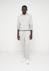 Szary bawełniany hoodie z przednią kieszenią i sznurkiem, w zestawie z dopasowanymi dresami. Całość dopełniają białe sneakersy.