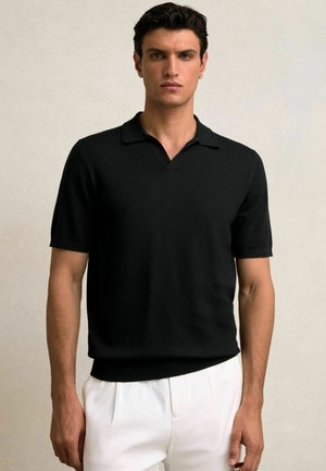 Czarna koszulka polo z krótkim rękawem wykonana z miękkiego dzianiny, z dekoltem w kształcie V i dopasowanym krojem. Połączona z jasnymi spodniami.