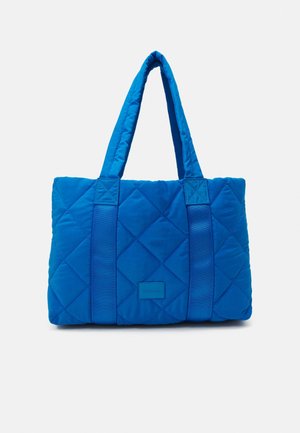 Sac cabas matelassé bleu vif avec doubles anses et détails de couture subtils sur fond blanc.